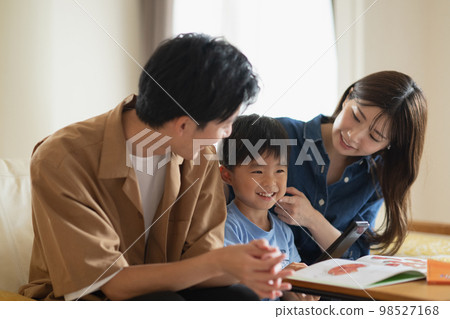 A smiling Japanese family sitting on the sofa, a family looking at a picture book A smiling Japanese family sitting on the sofa, a family looking at a picture book 98527168