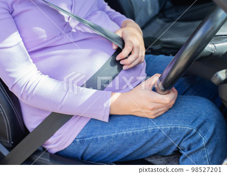 A pregnant woman wearing a seat belt drives a car. Safety and driving during pregnancy. 98527201