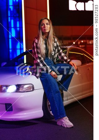 Young beautiful woman with straight long hair posing near white sport car in neon light Young beautiful woman with straight long hair posing near white sport car in neon light 98527283