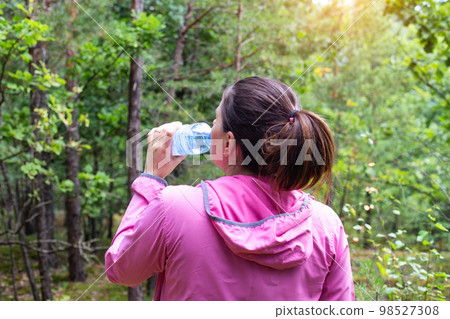 The girl drinks water in the forest on a summer sunny day. Survival in the forest, dehydration of the body. The girl drinks water in the forest on a summer sunny day. Survival in the forest, dehydration of the body. 98527308