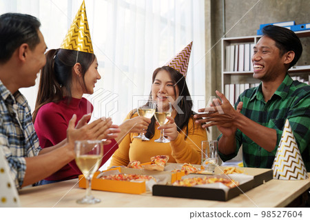 Friends at birthday party clinking glasses with champagne and pizza, enjoying Christmas vacation, pizza on the table. Holiday Party event. Friends at birthday party clinking glasses with champagne and pizza, enjoying Christmas vacation, pizza on the table. Holiday Party event. 98527604