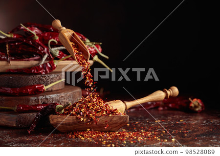 Chilli flakes are poured into a wooden dish. Chilli flakes are poured into a wooden dish. 98528089