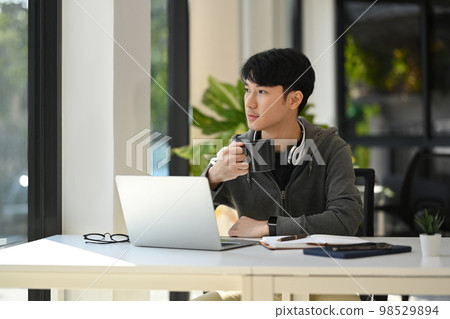 Thoughtful creative businessman drinking coffee, looking through window at modern office Thoughtful creative businessman drinking coffee, looking through window at modern office 98529894