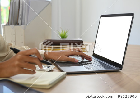 Cropped view of female employee hand typing on laptop computer and writing records to daily planner 98529909