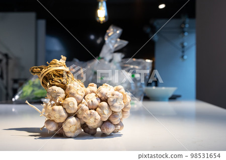 Garlic Bundle in studio light on the white marble surface table, prepare for a food demonstration behind. Garlic Bundle in studio light on the white marble surface table, prepare for a food demonstration behind. 98531654