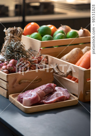 raw Pork is laid in front of vegetable, potato, carrot, shallot, lime, onion, tomato that in wood box. With studio light environment. raw Pork is laid in front of vegetable, potato, carrot, shallot, lime, onion, tomato that in wood box. With studio light environment. 98531828