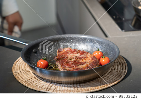 Cooked and grilled steak on pan with a little tomato with it, and take a break on a wicker plate for the next step. Cooked and grilled steak on pan with a little tomato with it, and take a break on a wicker plate for the next step. 98532122