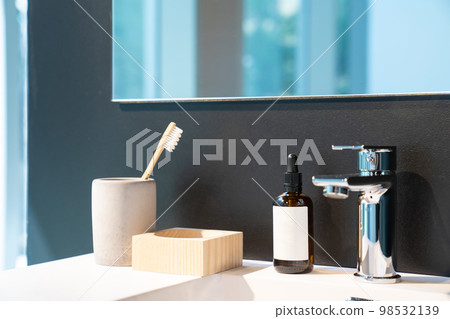 minimal toiletries such as toothbrush, serum bottle and wood storage on white sink and mirror on the black wall. minimal toiletries such as toothbrush, serum bottle and wood storage on white sink and mirror on the black wall. 98532139