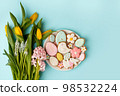 Beautiful tender Happy Easter card - seasonal tulip flowers and cute gingerbread cookies with sugar icing on white plate yellow background, glazed sweets for home party, banner, flyer 98532224