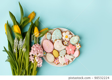 Beautiful tender Happy Easter card - seasonal tulip flowers and cute gingerbread cookies with sugar icing on white plate yellow background, glazed sweets for home party, banner, flyer 98532224