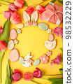 Sweets, pastry, gingerbread cookies for Easter table. Easter eggs, rabbit and tender simple flowers and tulips on yellow background, spring seasonal holiday wreath, banner for your site, flyer, coupon 98532229