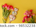 Sweets, pastry, gingerbread cookies for Easter table. Easter eggs heart shaped decor plate, pink tulips on yellow background top view copy space, spring seasonal holiday banner for site, flyer, coupon 98532238