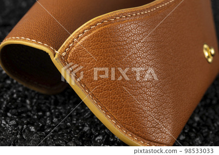 Part of a brown leather wallet or case with stitching. 98533033