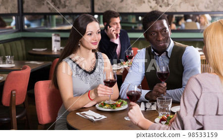 Cheerful pair with female friend at restaurant Cheerful pair with female friend at restaurant 98533159