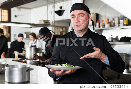Positive male cook with cooked dish in restaurant kitchen 98533434