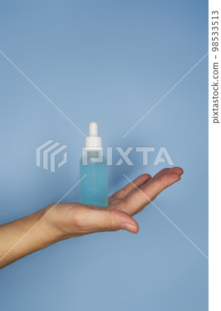 Female hands with serum in bottles on blue background Female hands with serum in bottles on blue background 98533513