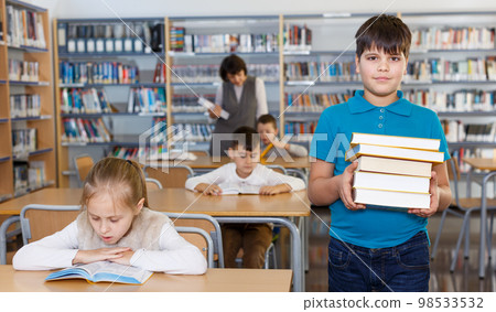 Smiling boy standing with pile of books Smiling boy standing with pile of books 98533532