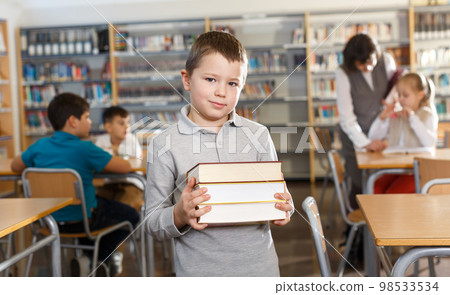 Smiling boy standing with pile of books Smiling boy standing with pile of books 98533534