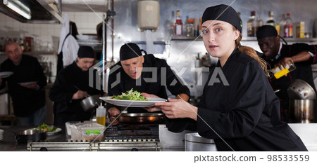 Positive female cook with cooked dish in restaurant kitchen 98533559