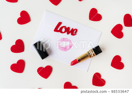 A white envelope with a lip print of red lipstick on a background of small red hearts. February 14 Valentine's Day concept. A white envelope with a lip print of red lipstick on a background of small red hearts. February 14 Valentine's Day concept. 98533647