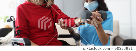 Doctor or nurse is training with woman with dumbbell both in protective masks at home Doctor or nurse is training with woman with dumbbell both in protective masks at home 98533951