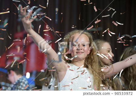Happy face of a little girl in falling confetti. Magic Time - Portrait of a very happy child with hands smiling while confetti falls. For a children's party or birthday. 98533972