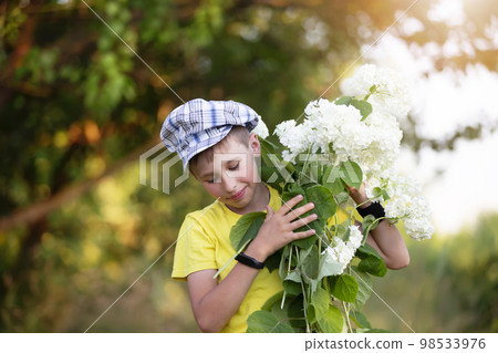 Cheerful happy village child with a bouquet of flowers. Smiling little boy with hydrangea in the garden. Mother's day, March 8, International Women's Day concept. Cheerful happy village child with a bouquet of flowers. Smiling little boy with hydrangea in the garden. Mother's day, March 8, International Women's Day concept. 98533976