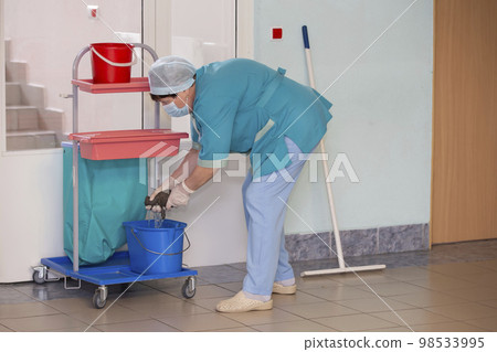 An adult female cleaner in uniform cleans the corridor of the hospital. 98533995