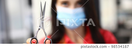 Woman hairdresser in protective mask holds scissors 98534187