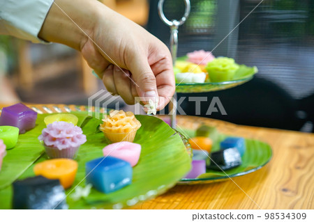 Thai Chef's hand is decorating Varieties traditional colorful Thai desserts set steaming flour, black custard, coconut custard and steaming bean, layer pudding cake 98534309