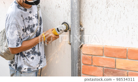 Asian worker young man sawing and kept detailed metal screw from a steel pole for preparing to install foam brick wall. 98534311