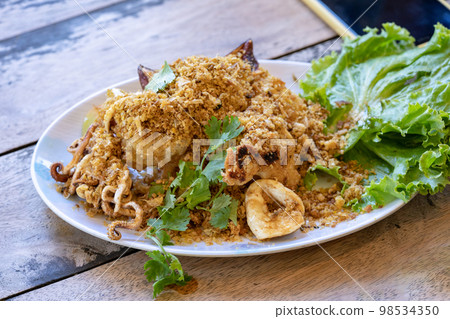 Fried squid with galic and coriander on top in white dish on wood table, ready to eat. 98534350