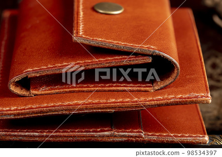 Part of a brown leather wallet or case with stitching. 98534397