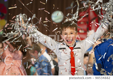 Happy little boy in confetti.Magic time - Portrait of a very happy child with hands smiling while falling confetti. At a children's party or birthday. Happy little boy in confetti.Magic time - Portrait of a very happy child with hands smiling while falling confetti. At a children's party or birthday. 98534882