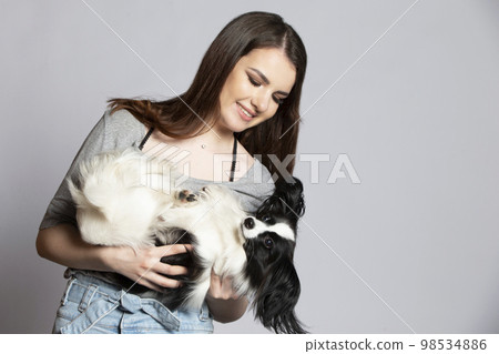 A cute young woman is hugging her papillon puppy. Love between owner and dog. Girl with dog studio portrait. A cute young woman is hugging her papillon puppy. Love between owner and dog. Girl with dog studio portrait. 98534886