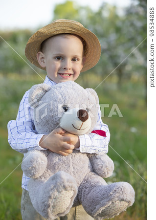 A happy child in a blooming garden holds a toy bear. A happy child in a blooming garden holds a toy bear. 98534888