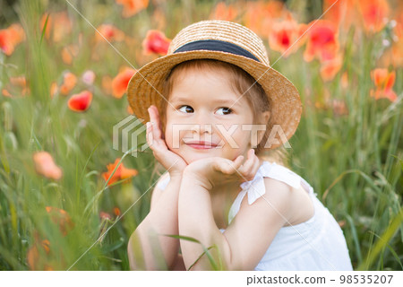 Cute funny baby girl 2-3 year old wear straw hat and white summer dress over flower meadow background. Kid laughing outdoors over nature Cute funny baby girl 2-3 year old wear straw hat and white summer dress over flower meadow background. Kid laughing outdoors over nature 98535207