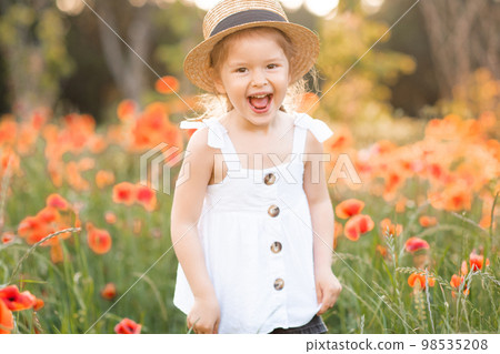 Cute funny baby girl 2-3 year old wear straw hat and white summer dress over flower meadow background. Kid laughing outdoors over nature Cute funny baby girl 2-3 year old wear straw hat and white summer dress over flower meadow background. Kid laughing outdoors over nature 98535208