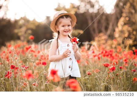 Cute funny baby girl 2-3 year old wear straw hat and white summer dress over flower meadow background. Kid laughing outdoors over nature Cute funny baby girl 2-3 year old wear straw hat and white summer dress over flower meadow background. Kid laughing outdoors over nature 98535210