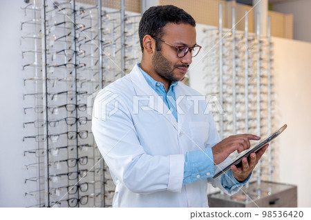 Male optometrist standing near the show-case with eyeglasses Male optometrist standing near the show-case with eyeglasses 98536420