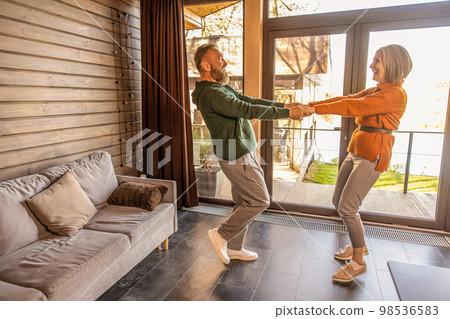 Happy couple dancing at home and looking energized and excited Happy couple dancing at home and looking energized and excited 98536583