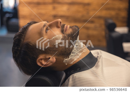 Headshot of a man sitting at the barbershop before shaving Headshot of a man sitting at the barbershop before shaving 98536648