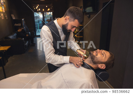 Professional barber carefully trimming the clients beard 98536662