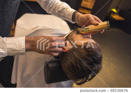 Professional barber carefully trimming the clients beard Professional barber carefully trimming the clients beard 98536676