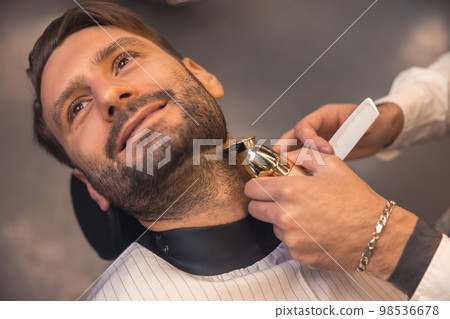 Barber trimming the clients beard Barber trimming the clients beard 98536678
