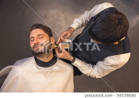 Barber trimming the clients beard Barber trimming the clients beard 98536680