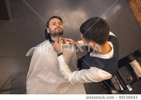 Barber trimming the clients beard 98536683