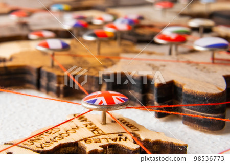 United Kindom flag on the pushpin with red thread showed the paths of movement or areas of influence in the global economy on the wooden map. Planning of traveling or logistic concept. Network United Kindom flag on the pushpin with red thread showed the paths of movement or areas of influence in the global economy on the wooden map. Planning of traveling or logistic concept. Network 98536773