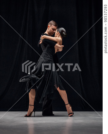 Man and woman, professional tango dancers performing in black stage costumes over black background. Couple dance 98537293