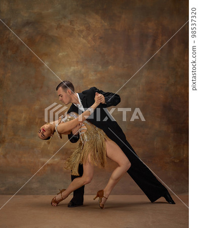 Man and woman, professional tango dancers in stylish, beautiful stage costumes performing over dark vintage background. Atrraction Man and woman, professional tango dancers in stylish, beautiful stage costumes performing over dark vintage background. Atrraction 98537320